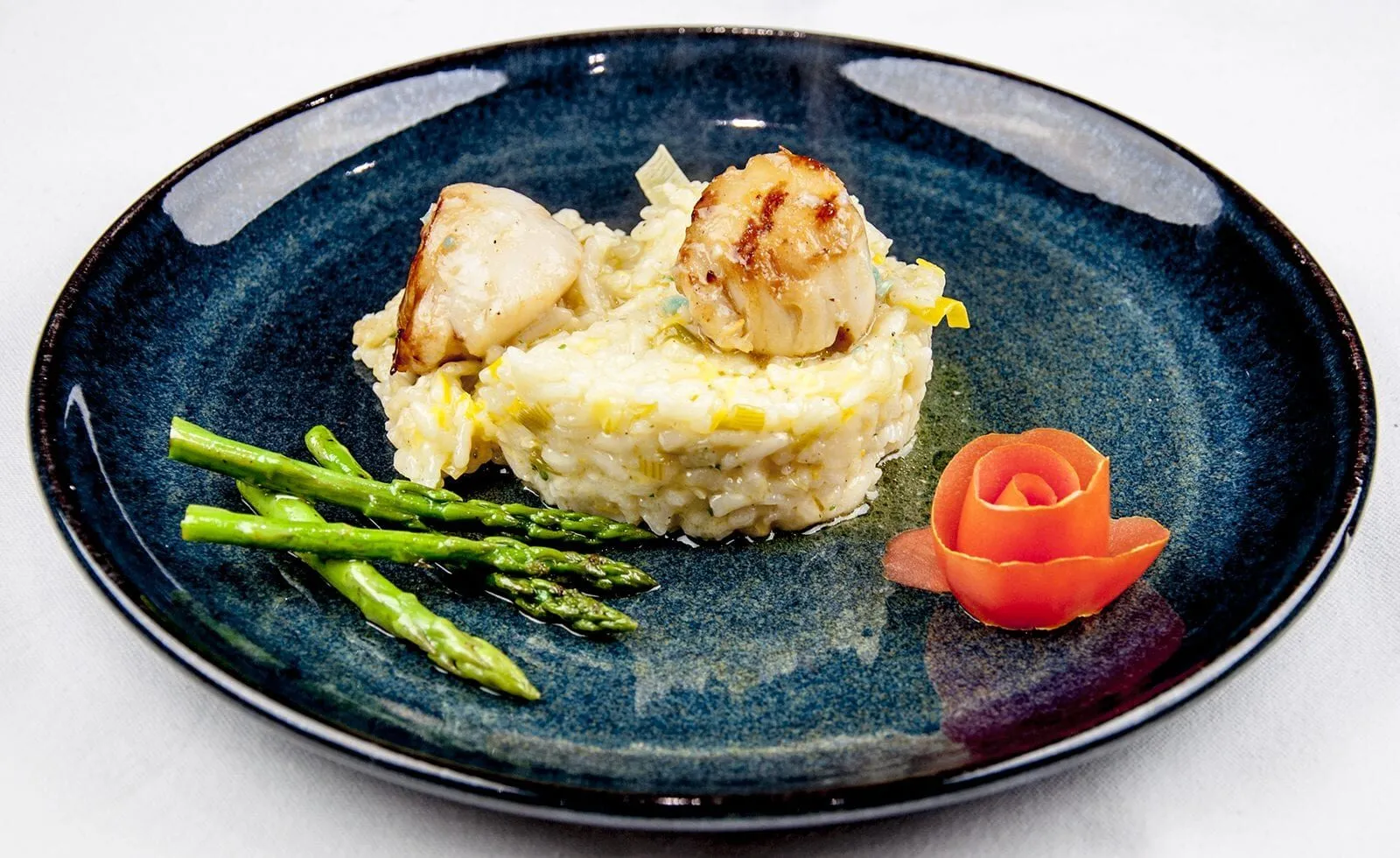 Pan fried scallops on a bed of leek risotto served with asparagus and garnished with a tomato rose | theyumyumclub