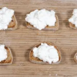 Add the ricotta to the crostini | https://theyumyumclub.com/2019/04/23/ricotta-prosciutto-fig-crostini/